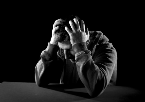 young desperate man suffering with hands on head in deep depression, pain , emotional disorder, grief and desperation concept isolated on black background with grunge studio lighting in black and white
